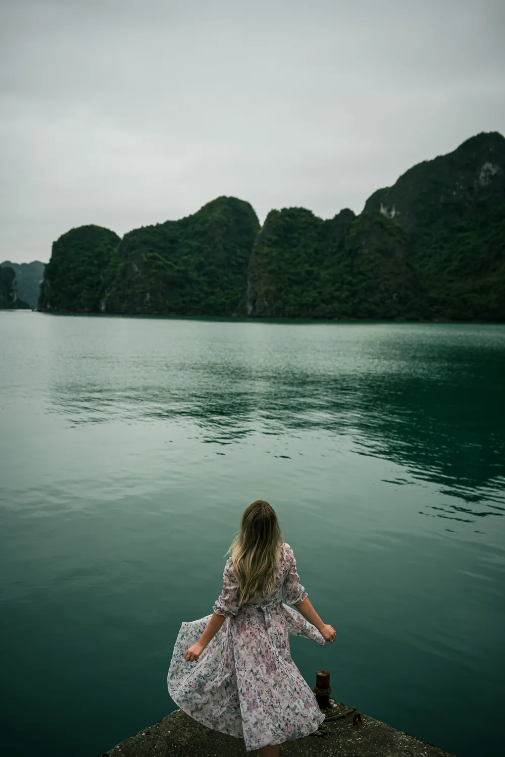 Perempuan bergaun di dermaga, menghadap teluk dan bukit karst saat mendung, dengan preset Digicam CCD